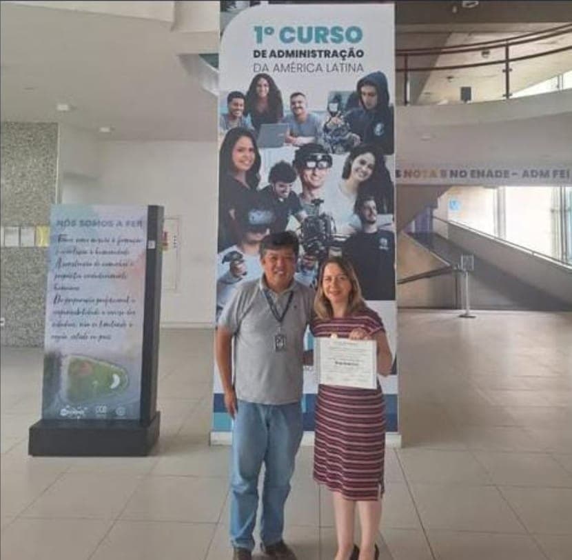 Profa. PhD Renata Correa segurando o certificado de doutorado ao lado do orientador, no Centro Universitário FEI